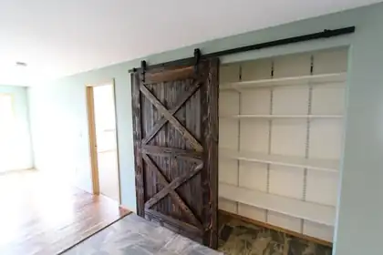 Rustic barn door on a black rail covering a wall of white shelves