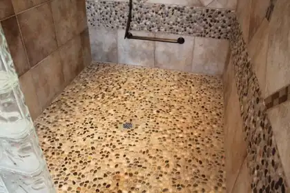 Walk-in shower with a pebble stone floor, a glass block wall on the left, tile walls and a grab bar