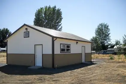 New detached building with a metal roof, white and tan siding, and two entry doors