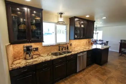 Kitchen with dark cabinets, glass-front uppers, and a stone tile backsplash