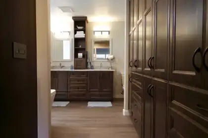 Bathroom with a double sink dark wood vanity, two mirrors, a tall linen cabinet and a wall of dark paneled storage cabinets