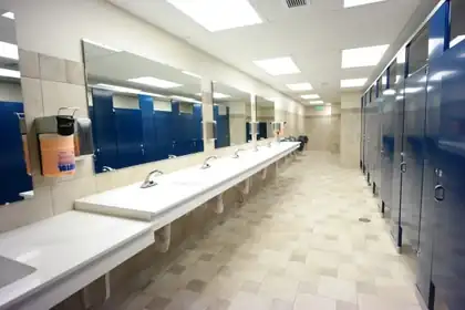 Commercial restroom with a long white sink counter, large mirrors, blue stall partitions and a tile floor