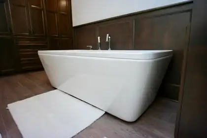 Freestanding white tub against a dark wood paneled wall