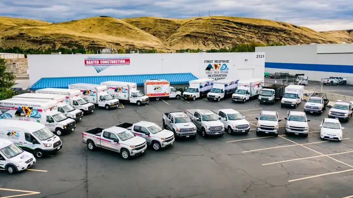 Baxter Construction's fleet of branded trucks and vans lined up in front of the River Road building in Yakima, with the hills behind