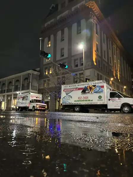 Two Baxter trucks parked downtown at night on wet pavement during a call-out