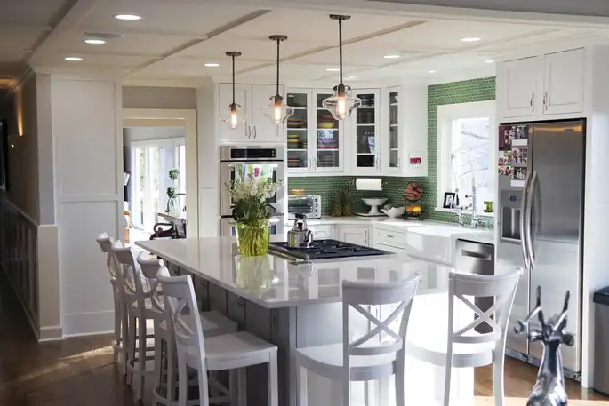 Open kitchen remodel with white cabinets, a green tile backsplash, glass pendant lights over a long island with white bar stools, and a stainless refrigerator