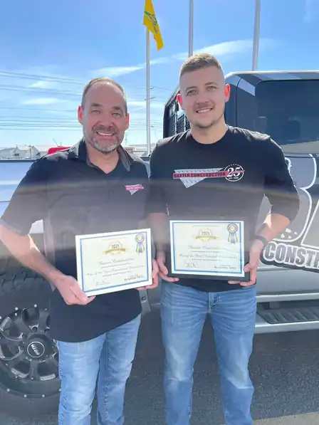 Brice and Tyler Baxter holding certificates beside a Baxter truck