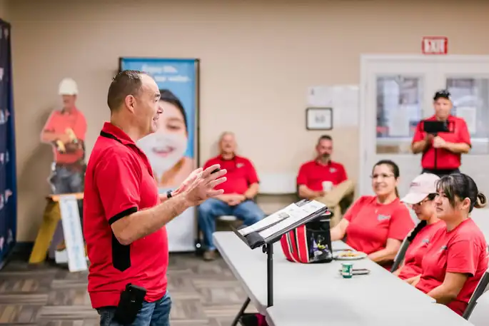 A trainer addressing a room of Baxter staff in red company shirts during a training meeting